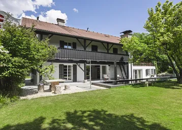 Haus mit großem Garten, Terrasse und langem Pool unter blauem Himmel.