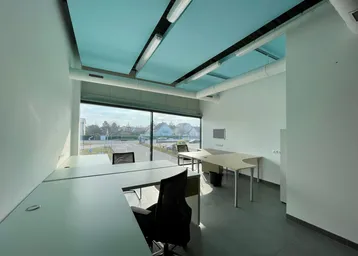 Modernes Büro mit großen Fenstern, hellblauen Deckenpaneelen und grauem Fliesenboden, bietet viel Tageslicht.