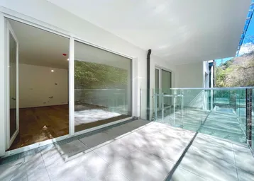 Heller Balkon mit Fliesenboden und Glasgeländer, bietet Zugang zu einem leeren Raum.