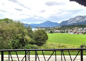 Blick vom Balkon auf einen malerischen See, majestätische Berge und eine idyllische Landschaft mit Dorf.