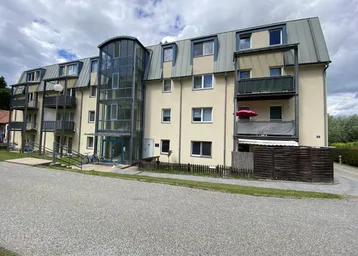 Mehrstöckiges Wohngebäude mit Balkonen und modernem Glasaufzug an der Fassade.