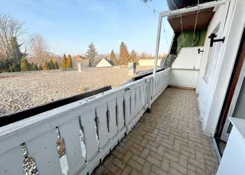 Heller Balkon mit weißem Holzgeländer und weitem Blick über die Dächer und Bäume.