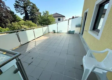 Große geflieste Terrasse mit Milchglasgeländer und Blick ins Grüne, ideal zum Entspannen.