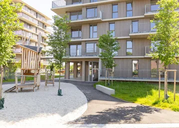 Moderner Wohnkomplex mit Holzfassade und Kinderspielplatz im Außenbereich.