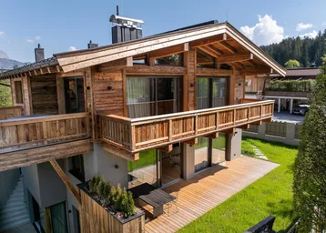 Modernes Chalet mit Holzbalkonen, großer Holzterrasse und gepflegtem Rasen.
