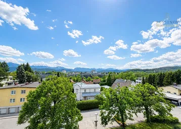 Weitläufiger Blick über die Stadt und die umliegende Berglandschaft unter blauem Himmel.