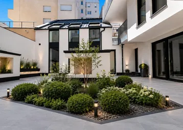 Innenhof mit gepflegter Gartenanlage, modernen Pflanzen und Beleuchtung, umgeben von Gebäudefassaden.