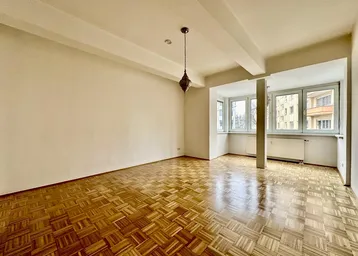 Heller, leerer Wohnraum mit klassischem Parkettboden, großen Fenstern und Stadtblick.