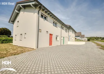 Moderne Reihenhäuser mit heller Fassade und gepflasterter Zufahrt unter blauem Himmel.