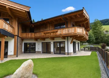 Neubau-Chalet mit Holzfassade, großzügiger Terrasse und gepflegtem Rasenbereich unter blauem Himmel.