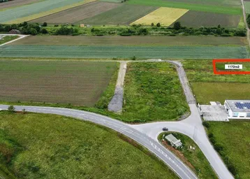 Luftaufnahme eines Grundstücks von 1172m² umgeben von Feldern und einer Straße mit einem Gebäude mit Solaranlage.