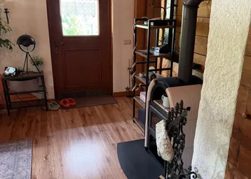 Wohnzimmer mit Holzboden, Kaminofen und Zugang zur Haustür, gemütlich eingerichtet.