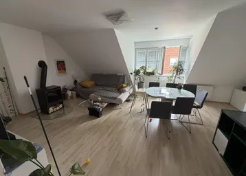 Helles Dachgeschoss-Wohnzimmer mit Kaminofen, Esstisch und schrägen Wänden.