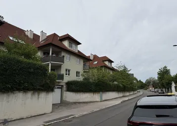 Mehrfamilienhaus mit Satteldach, Balkonen und gepflegter Hecke entlang der Straße.