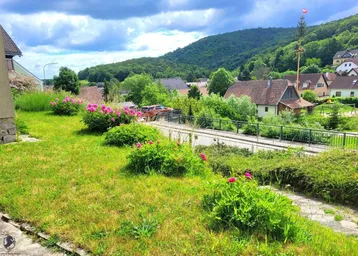 Gartenblick auf die umliegende Hügellandschaft und die darunter liegende Straße mit weiteren Häusern.
