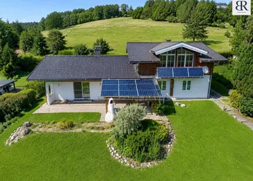 Haus mit Solaranlage, gepflegtem Garten und weitem Blick auf die grüne Hügellandschaft.