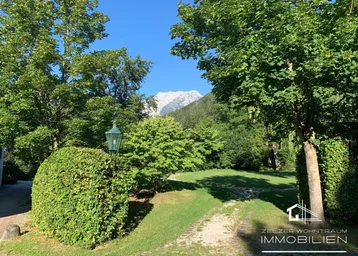 Grüner Gartenbereich mit gepflegtem Rasen, Hecken und Bergblick im Hintergrund.