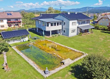 Luftaufnahme des Hauses mit großem Garten, Teich und Bergblick unter blauem Himmel.