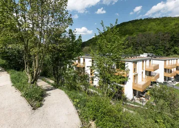 Moderne Wohngebäude in grüner Hügellandschaft mit Wegen und üppiger Vegetation.