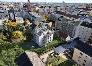 Luftaufnahme der Wohnanlage in einer grünen Stadtlandschaft mit umliegenden Gebäuden und viel Baumbestand.