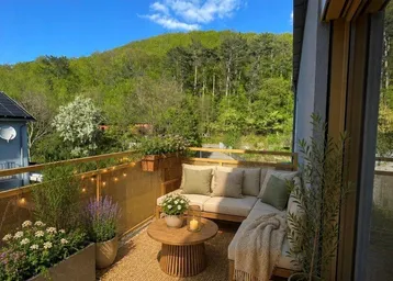 Heller Balkon mit gemütlicher Sitzecke, vielen Pflanzen und weitem Blick ins Grüne.
