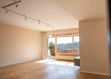 Helles Wohnzimmer mit Fischgrätparkett und Zugang zum Balkon, durchflutet von Sonnenlicht.