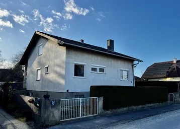 Einfamilienhaus mit heller Fassade und Satteldach unter blauem Himmel.
