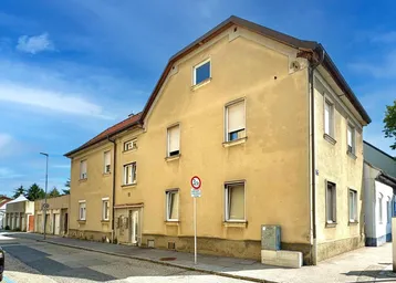 Gebäudeansicht von der Straße mit hellgelber Fassade und mehreren Fenstern unter blauem Himmel.