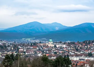 Panoramablick auf eine Stadt mit blauen Bergen im Hintergrund unter bewölktem Himmel.