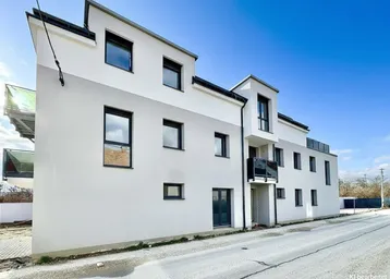 Modernes Mehrfamilienhaus mit weißer und grauer Fassade unter blauem Himmel.