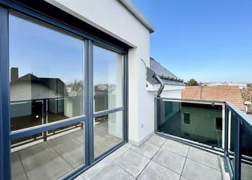 Moderner Balkon mit Glasgeländer und Schiebetür, bietet einen Blick auf die umliegenden Dächer.