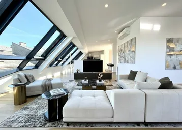 Helles, modernes Wohnzimmer mit großen Dachfenstern, offenem Grundriss und Blick über die Dächer.
