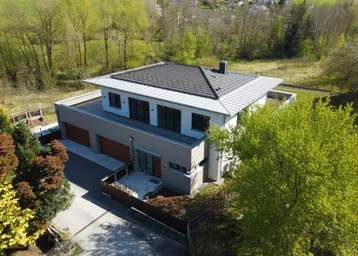 Luftaufnahme eines modernen Einfamilienhauses mit Satteldach und Photovoltaikanlage in grüner Umgebung.