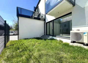 Kleiner Gartenbereich mit Rasenfläche und Blick auf die moderne Fassade des Gebäudes.