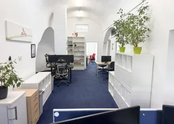 Helles Büro mit gewölbten Decken, blauem Teppichboden und modernen Arbeitsplätzen.