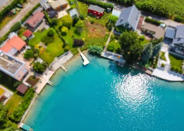 Luftaufnahme eines Grundstücks am See mit umliegenden Häusern und einem kleinen Steg.