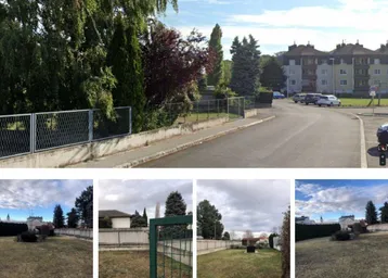 Blick auf die Straße und umliegende Wohngebäude mit einem eingezäunten Grundstück im Vordergrund.
