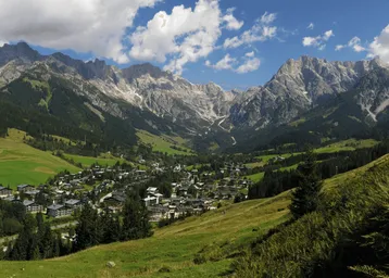 Panoramablick auf ein malerisches Dorf in einem Tal, umgeben von majestätischen Bergen und grünen Wiesen.