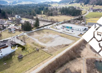 Luftaufnahme eines großen Baugrundstücks in ländlicher Umgebung mit angrenzendem Gewerbegebiet und Bergblick.