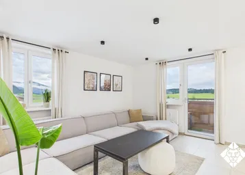 Helles Wohnzimmer mit großem Sofa, Blick ins Grüne und Zugang zum Balkon.