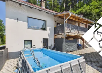 Hausfassade mit einem aufgestellten Pool im Garten und einem Balkon mit dekorativem Geländer.