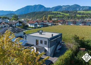 Luftaufnahme eines modernen Gebäudes mit Flachdach und Photovoltaikanlage in ländlicher Umgebung.