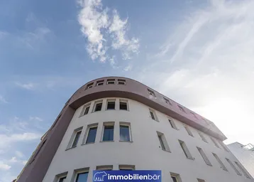 Moderne Gebäudefassade mit geschwungenen Linien und zahlreichen Fenstern unter blauem Himmel.