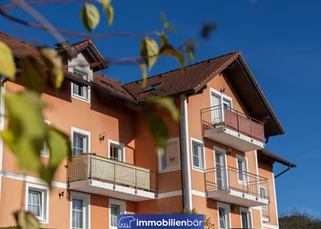 Gebäude mit oranger Fassade, Satteldach und mehreren Balkonen unter blauem Himmel.