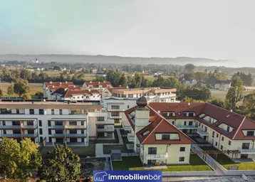 Luftaufnahme eines modernen Wohnkomplexes mit traditionellem Gebäude und grüner Umgebung.