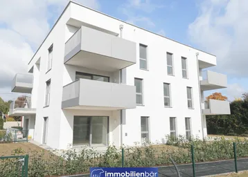 Modernes Mehrfamilienhaus mit weißer Fassade und mehreren Balkonen unter blauem Himmel.