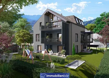 Modernes Mehrfamilienhaus mit Balkonen, Terrassen und einem Kinderspielplatz im grünen Außenbereich.