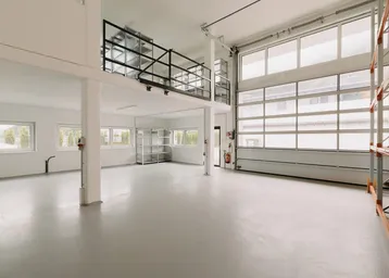 Geräumige Lagerhalle mit hohen Decken, Betonboden und einem Rolltor, inklusive einer oberen Galerie.