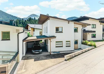 Weißes Einfamilienhaus mit Carport und Bergblick in ländlicher Umgebung.