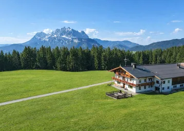 Traditionelles Landhaus in alpiner Umgebung mit weiten Wiesen und beeindruckendem Bergblick.